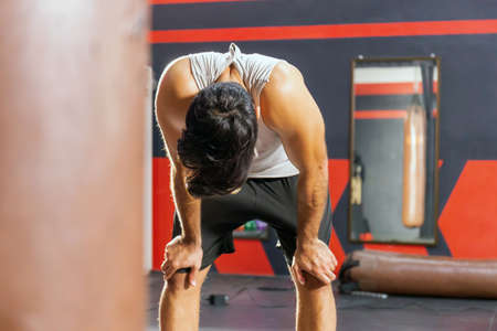Tired man having rest after workout. Young athletic man in sportswear looking exhausted while standing at gymの写真素材