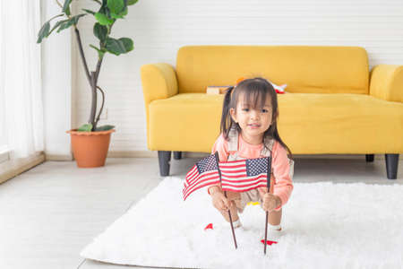 Cute little girl with a small national flag of United States, kid girl playing in living roomの写真素材