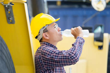 Worker man in hard hat drinking water at containers cargoの写真素材