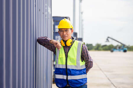 Relaxing engineer man in industry containers cargo, Foreman dock worker in hardhat and safety vest control loading containers box from cargoの写真素材