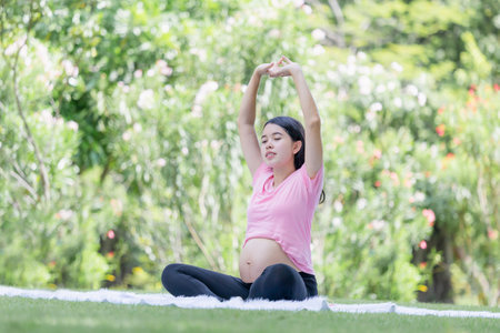 Cheerful pregnant woman sitting relax in the park and stretching musclesの写真素材