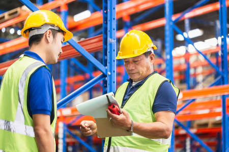 Workers team taking inventory in factory warehouse, Manual workers working in warehouse talking about jobの写真素材