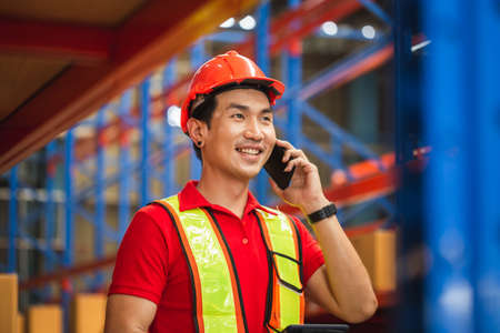 Cheerful warehouse worker with smartphone and digital tablet checking inventory in warehouse, Worker man working in warehouseの写真素材