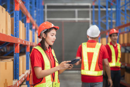 Female factory manager using digital tablet in a warehouse, Warehouse workers group in aisle between rows of tall shelves full of packed boxesの写真素材