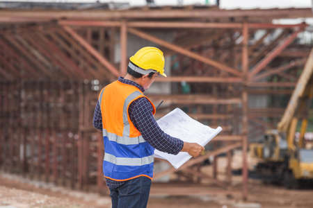 Asian construction engineer checking project at the building site, Architect with a blueprints at a construction site, Foreman worker in hardhat at the infrastructure construction siteの写真素材