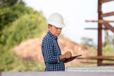 Engineer man checking project at building site, Foreman in hardhat with digital tablet at infrastructure construction siteの写真素材