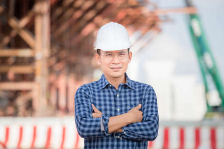 Worker man with arm crossed looking at camera, Engineer checking project at building site, Man in hardhat at infrastructure construction siteの写真素材