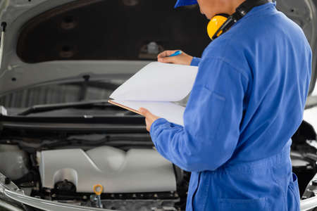 Auto mechanic holding clipboard checklist the car at mechanic shop, Mockup blank clipboard, Technician doing the checklist for repair machine a car in the garageの写真素材