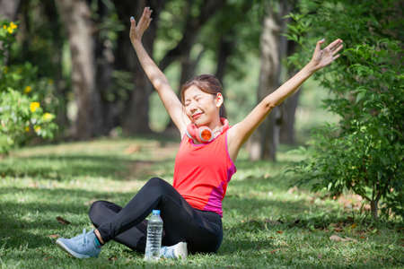 Sport woman breathing deeply fresh air with arms raised outdoor in urban park with blurred backgroundの写真素材