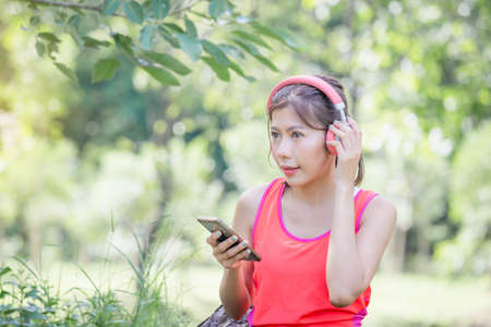 Young beautiful sportswomen in headphones with mobile smartphones at summer green parksの写真素材