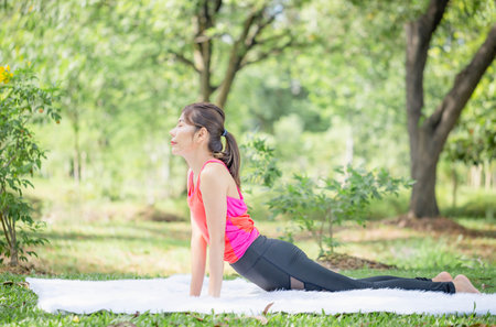 Young woman doing exercises in yoga pose in the park, Side view of slim sportswoman doing stretching exercise at summer green parksの写真素材