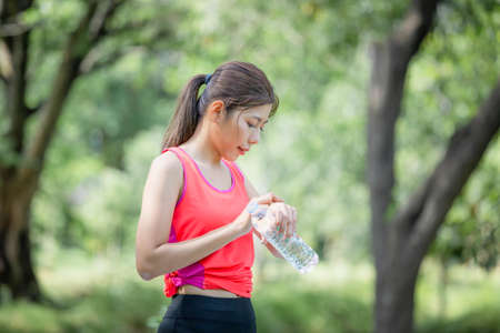 Young beautiful woman with plastic water bottle looking smartwatch and smartphone, Sport woman at summer green parksの写真素材