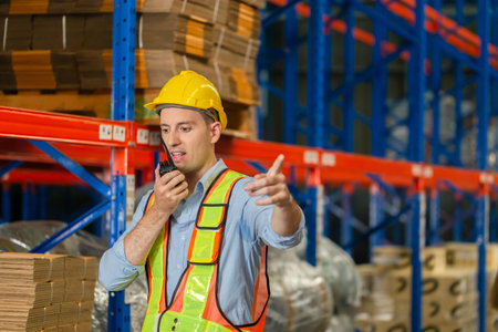 Warehouse worker working in factory warehouse industry and using radio talking communication, Foreman in hardhat safety vest with Two-Way radio working in logistics centerの写真素材