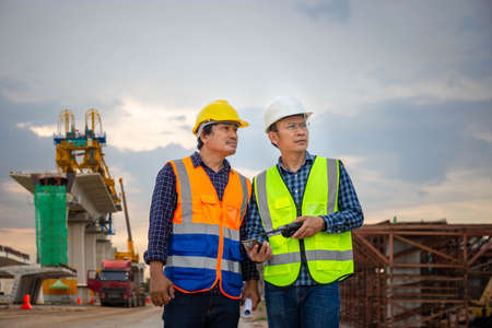 Engineer and builders in hardhats discussing on infrastructure construction site, Engineer and foreman worker checking project at building site, Teamwork conceptsの写真素材