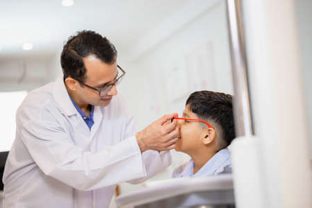 Boy doing eye test checking examination with optometrist using trial frame in optical shop, Smiling Indian-thai boy choosing glasses in optics storeの写真素材