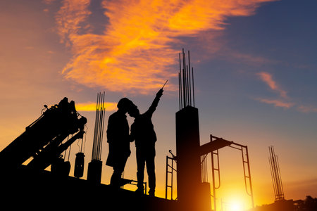 Silhouette of Engineer and worker checking project at building site background, construction site at sunset in evening timeの写真素材