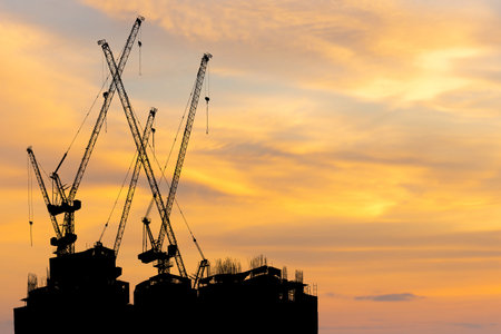 Silhouettes of building construction site and construction cranes with clipping path sunset backgroundの写真素材