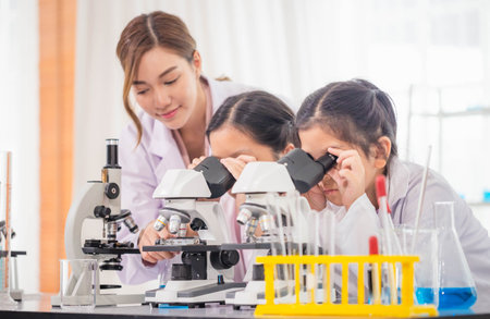 Elementary science class, Child girl looking at slides in through microscope, Science laboratory,...