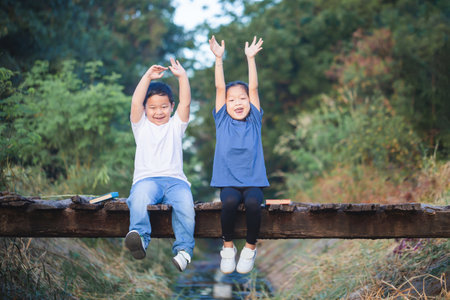 Cheerful children sitting on wooden bridge, Happy kids boy and girl having fun outdoor, brother and sister playing in gardenの写真素材
