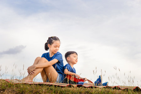 Happy boy and girl with guitar having fun outdoor, Portrait of adorable brother and sister playing outdoors. Asian kids singing songs in the gardenの写真素材