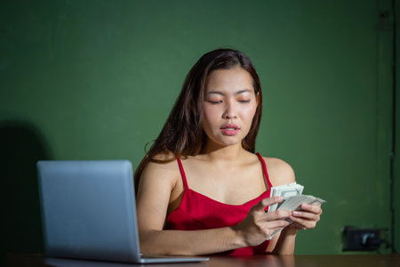 Young woman working online on laptop computer and showing money dollar bills banknotes