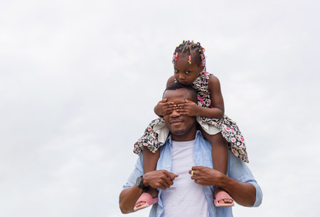 Cheerful African American father and daughter, Father carrying daughter on shoulders, Little girl on the shoulders of her dadの写真素材