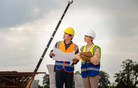 Female engineer and foreman worker checking project at building site, Engineer and builders in hardhats discussing on construction site, Teamwork conceptsの写真素材