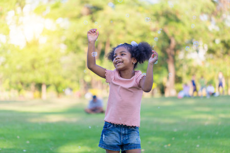 Happy kid girl playing with soap bubbles. Active child playing outdoor in the park.の写真素材