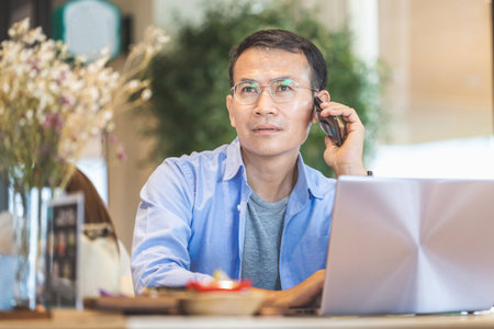 Asian man using smartphone and laptop in coffee shop, Hands typing on laptop, Technology in use conceptsの写真素材