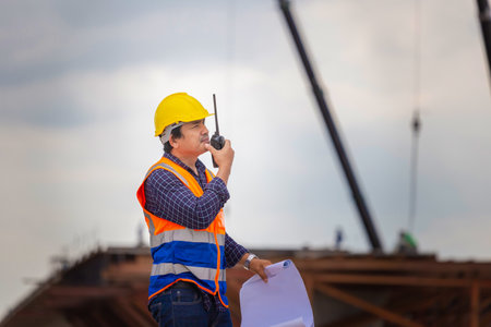 Construction engineer checking project at the building site, Architect with a blueprints at a construction site, Foreman worker in hardhat at the infrastructure construction siteの写真素材