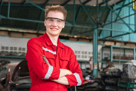 Portrait of a young car mechanic crossed hands standing in a repair garage, Car repair and maintenance conceptsの写真素材