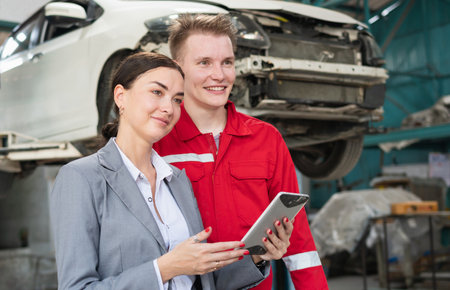 Female manager and car mechanic while working in auto repair shop, Woman at a car garage getting mechanical service, Car repair, and maintenance conceptsの写真素材