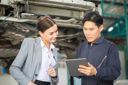 Mechanic and young woman client talking together at the repair garage, Female manager and auto mechanic in auto repair shop, Car repair and maintenance conceptsの写真素材