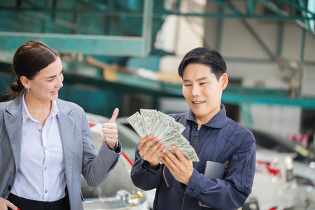 Female customers paying mechanics with cash at the repair garage, Customer and mechanic in auto repair shops, Car repair and maintenance conceptsの写真素材