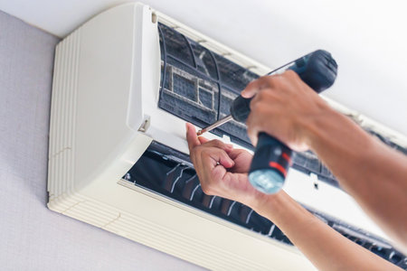 Repairman using a screwdriver fixing modern air conditioner, Male technician cleaning air conditioner indoors, Maintenance and repairing conceptsの写真素材