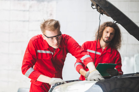 Young Caucasian car mechanic with a checklist, Mechanics in uniform are working in auto service, Technician checking modern car at garage, Car repair and maintenance conceptsの写真素材