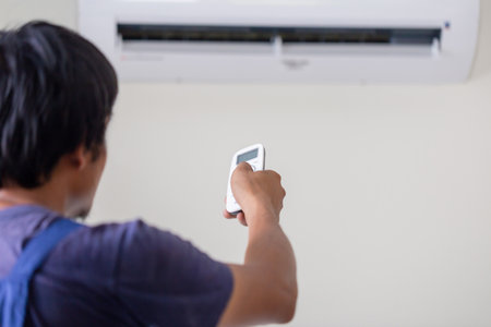 Air conditioner inside the room with technician operating remote controller, Repairman fixing air conditioner unit, Maintenance and repairing conceptsの写真素材