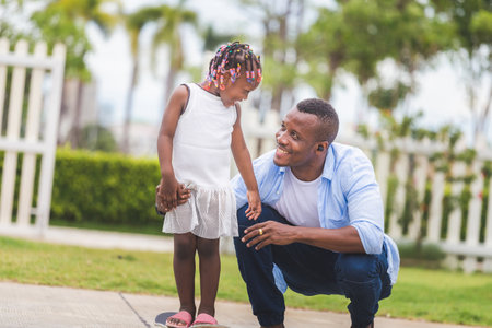 Father's day concept, Father helping her little daughter to ride a skateboard, Little girl and her father playing with skateboard outdoorsの写真素材