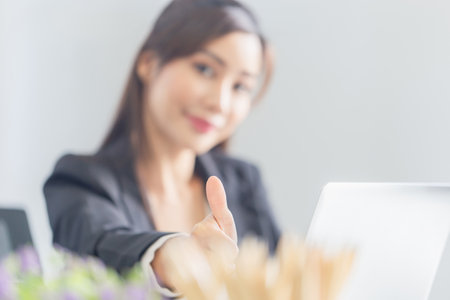 Selective focus of young Asian business woman showing thumbs up and looking at cameraの写真素材