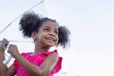 Cheerful child girl with an umbrella playing with rain in the park, Cute little kid girl playing outdoors in the gardenの写真素材