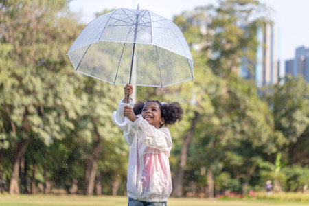 Cheerful child girl with an umbrella playing with rain in the park, Cute little kid girl playing outdoors in the gardenの写真素材