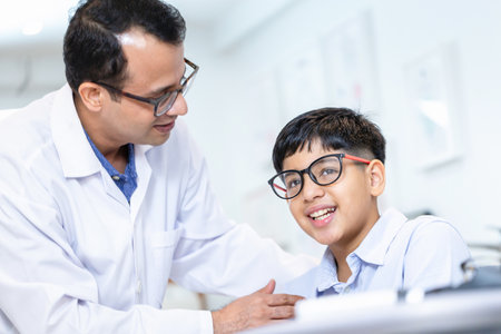 Boy doing an eye test checking examination with optometrist in the optical shop, Smiling Indian-thai boy choosing glasses in an optics storeの写真素材