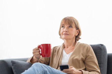 Portrait of Relaxing woman with cups of coffee on cozy sofa in the living room, Mature woman using...