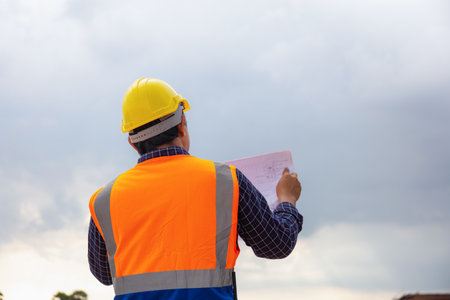 Engineer man with blueprint checking project at building site, Foreman worker in hard hats on construction siteの写真素材