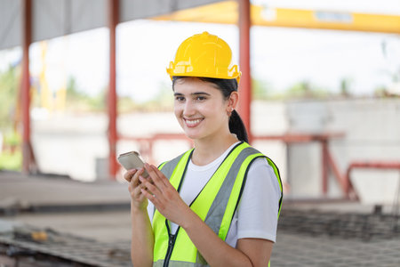 Cheerful female engineer in the hard hat uses mobile phone, Industrial worker using mobile...