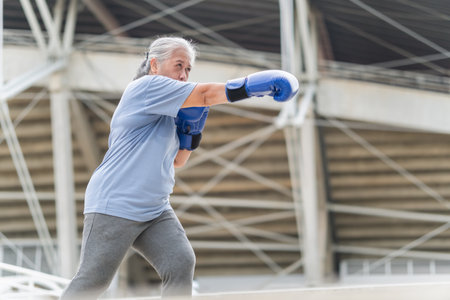 Asian senior sportswoman boxing while working out outdoors