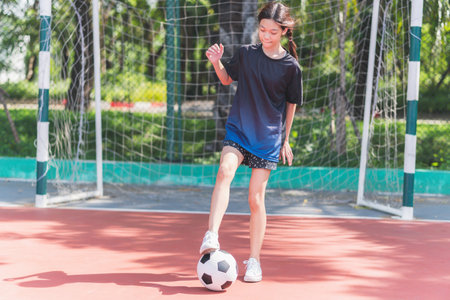 Asian child girl playing football in the urban outdoor futsal court