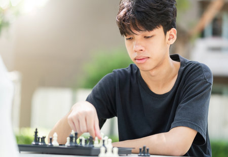 Asian teenage boy playing chess board, Asian boy relaxing hobbies playing a game of chess outdoor