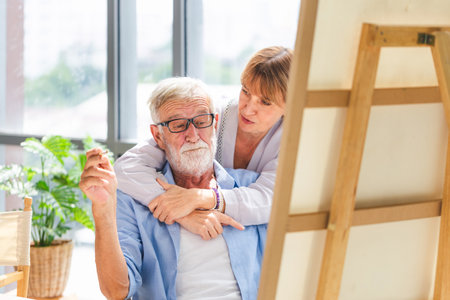 Cheerful senior couple spending time together in the living room, Happy senior couple painting on a canvas in living room, Caucasian couple drawing on a canvas, Happy retirement conceptsの写真素材