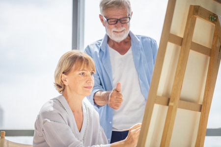 Senior couple spending time together in the living room, Happy senior couple painting on a canvas in living room, Caucasian couple drawing on a canvas, Happy retirement conceptsの写真素材